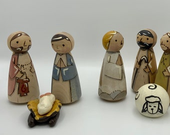 May include: A nativity scene set with wooden figurines of Mary, Joseph, a baby Jesus in a manger, and three shepherds. There are also five white wooden sheep with black painted faces.
