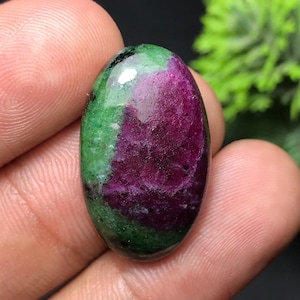 Puede incluir: Una gema ovalada con una vibrante combinación de colores. La piedra presenta un centro magenta intenso, rodeado por una banda de verde intenso. La superficie pulida refleja la luz, resaltando los patrones naturales y texturas de la piedra.