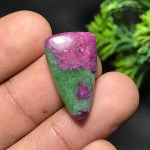 Op de afbeelding: Een gepolijste edelsteen met een driehoekige vorm. De bovenste helft is diep magenta, overgaand in levendig groen aan de onderkant. De steen heeft een glad, reflecterend oppervlak.