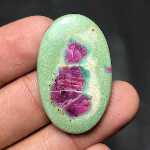 Può includere: Gemma ovale con una base verde chiaro e un motivo centrale irregolare di tonalità rosa intenso e magenta. La pietra lucida mostra variazioni di colore e texture naturali.