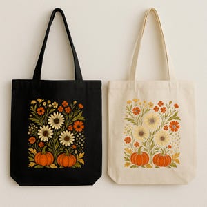 May include: Two tote bags, one black and one cream, each featuring a floral design with sunflowers, orange flowers, and pumpkins. The black bag has a black handle, while the cream bag has a cream handle. The design is a fall-themed illustration.