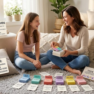 Pu&ograve; includere: Una madre e una figlia giocano a un gioco di carte, sorridendo e ridendo. Il gioco include carte con argomenti come "Amicizie" e "Immagine corporea". La scatola dice "Teen Conversation Starter Cards" e "160 carte".