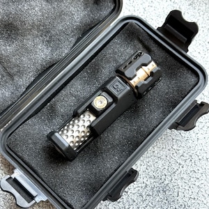 May include: A black and gold flashlight with a textured grip and a metal end. The flashlight is in a black case with foam padding. The flashlight has the text "P5" and "MAYICE 2022" on it.