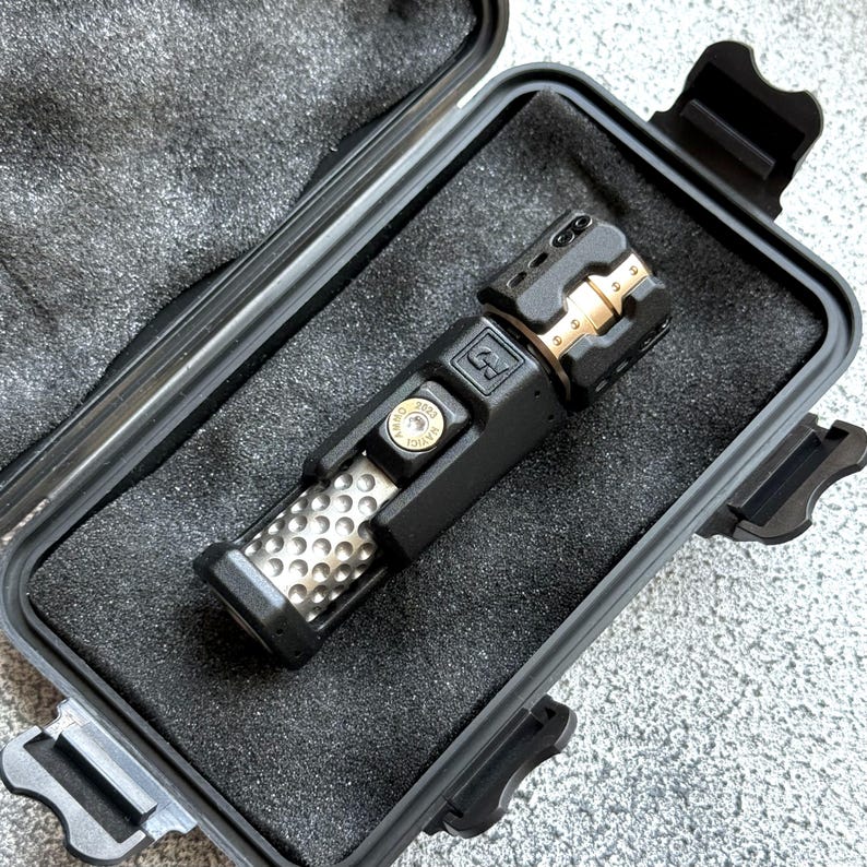 May include: A black and gold flashlight with a textured grip and a metal end. The flashlight is in a black case with foam padding. The flashlight has the text "P5" and "MAYICE 2022" on it.