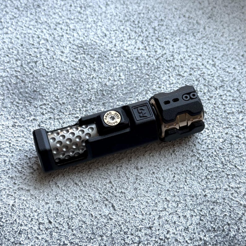 May include: A black and gold flashlight with a textured metal end and a perforated metal sleeve. The flashlight has a button with the text "AMMO 2023 MAYIC" and the letter "R" on the side.