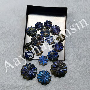 May include: A collection of faceted, starburst-shaped gemstones in shades of blue, gold, and brown. The gemstones are arranged on a small, rectangular metal tray, with some scattered around it. The gemstones have a polished, reflective surface.