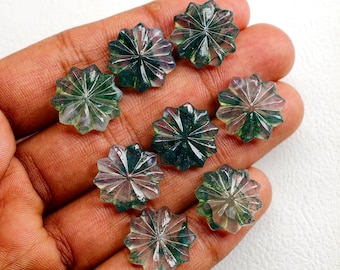 May include: A collection of eight star-shaped gemstones with intricate carved facets. The gems display a mix of clear, green, and purple hues. The gemstones are held in a hand, showcasing their size and detail. These gemstones are ideal for jewelry making.