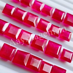 May include: Rows of square-cut, vibrant red gemstones. Each gem has a faceted, lighter-colored center, creating a contrast against the deep red hue. The gems are arranged in neat rows, showcasing their polished surfaces.