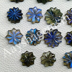 May include: Close-up of several star-shaped labradorite gemstones. The gemstones have a carved design with blue, green, and gold iridescent colors. The gemstones are arranged on a light-colored surface.