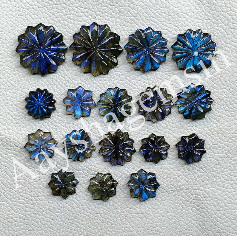 May include: A collection of carved labradorite gemstones in various sizes. The gemstones are shaped like flowers with intricate petal details. The colors range from deep blues and greens to iridescent flashes, set against a neutral background.