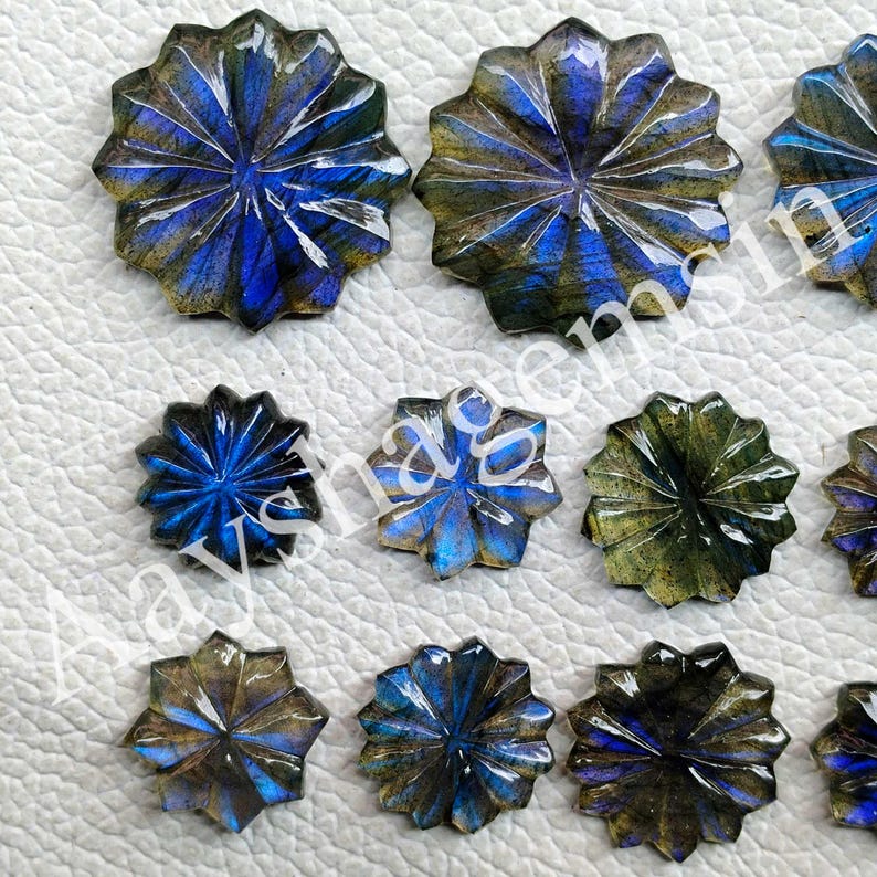 May include: A collection of carved labradorite gemstones. The gemstones are starburst-shaped with a mix of blue, green, and gold iridescence. The carved facets create a radial pattern, enhancing the stones' natural shimmer.