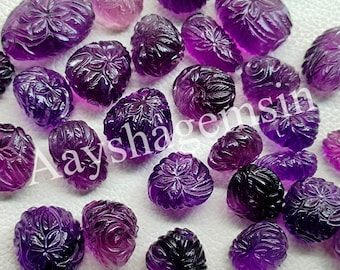 May include: A collection of carved amethyst gemstones in various shades of purple. Each gemstone is intricately carved with a floral design. The gemstones are scattered across a surface, showcasing their detailed craftsmanship and color variations.