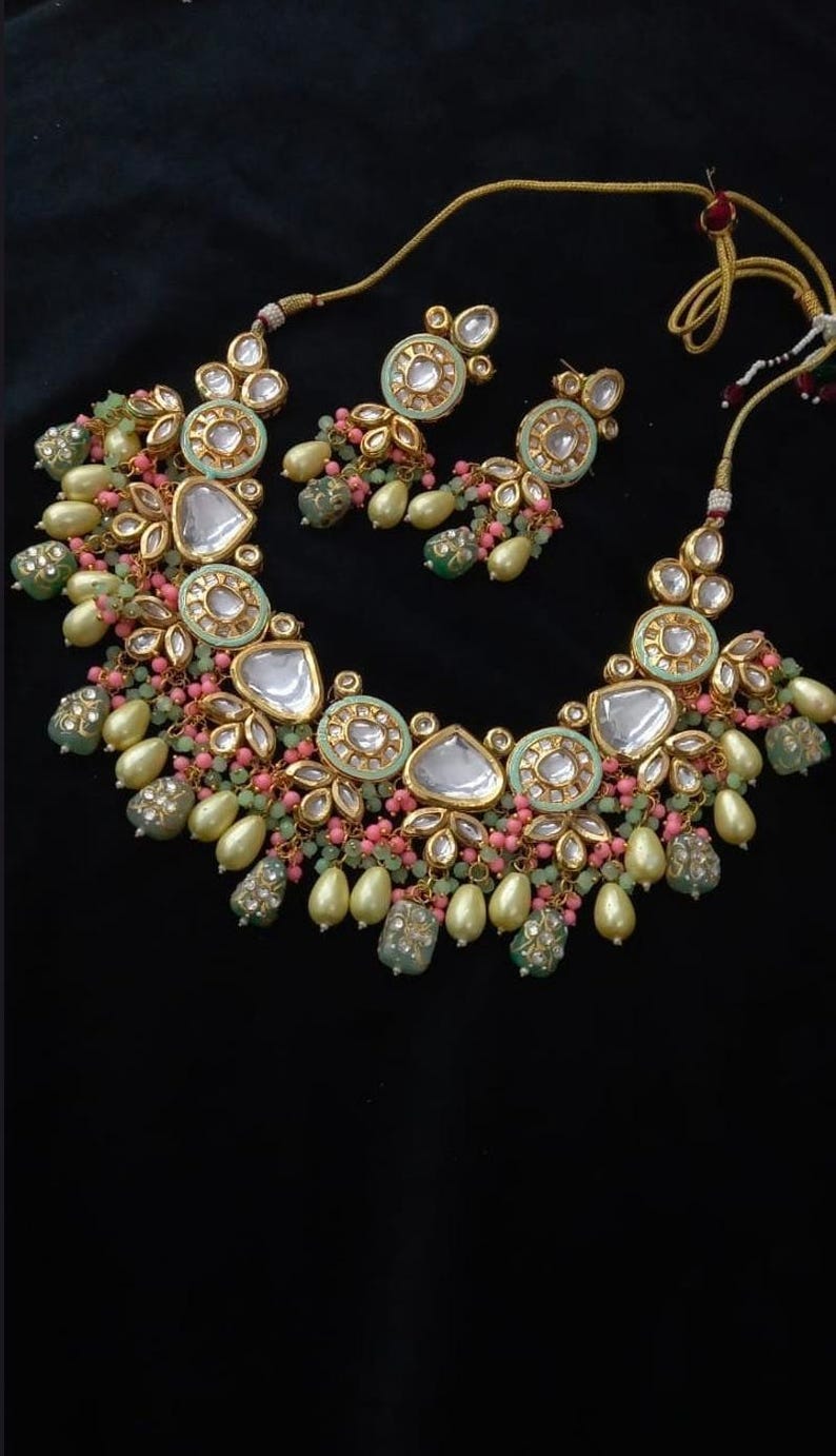 Puede incluir: Un conjunto de collar y pendientes en tono dorado con una combinaci&oacute;n de colores verde menta, rosa y crema. El collar presenta piedras grandes y transparentes en forma de l&aacute;grima y piedras redondas m&aacute;s peque&ntilde;as. Los pendientes reflejan el dise&ntilde;o del collar.