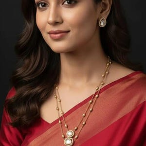 Peut inclure: Une femme portant un collier en or avec trois pendentifs en forme de goutte et des boucles d'oreilles assorties. Le collier a une double rangée de petites perles d'or. Elle porte un sari rouge.
