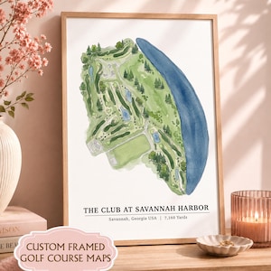 May include: A framed watercolor print of The Club at Savannah Harbor golf course map in Savannah, Georgia, USA, featuring 7,160 yards. The map displays green fairways, sand traps, and a large blue body of water in a light wood frame.