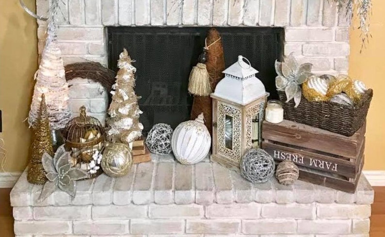 Pu&ograve; includere: Un camino in mattoni bianchi decorato per le festivit&agrave; con una variet&agrave; di ornamenti, tra cui una gabbia per uccelli, una lanterna e una cassa di legno con il testo "Farm Fresh".