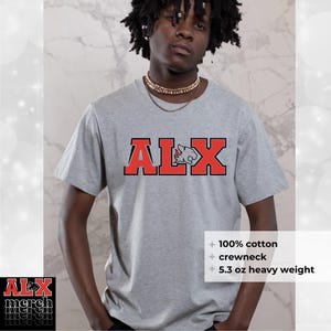 May include: A gray crewneck t-shirt with the red text "ALX" and a bull graphic. The shirt is made of 100% cotton and is 5.3 oz heavy weight. The shirt is being worn by a person.