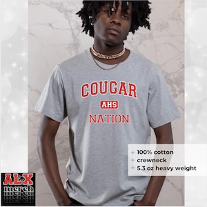 May include: A gray crewneck t-shirt with the text "COUGAR AHS NATION" in red lettering. The shirt is made of 100% cotton and is a 5.3 oz heavy weight. The shirt is a crewneck style.