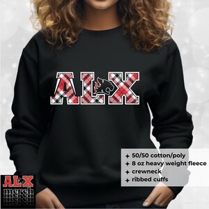 May include: Black sweatshirt with the letters "ALX" in a red and black plaid pattern. The letter "L" features a cougar graphic. The sweatshirt has a crewneck and ribbed cuffs. The text "ALX merch merch merch" is in the lower left corner.