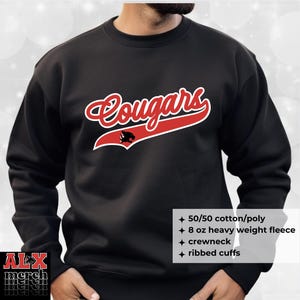 May include: Black crewneck sweatshirt with the word "Cougars" in red script with a white outline. A black cougar head is on the red banner. The sweatshirt has ribbed cuffs and is made of 50/50 cotton/poly 8 oz heavy weight fleece.