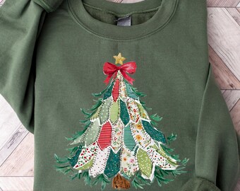 May include: Green sweatshirt featuring an embroidered Christmas tree design. The tree is decorated with colorful fabric patches, a red bow, and a gold star. The sweatshirt has long sleeves and a crew neck.
