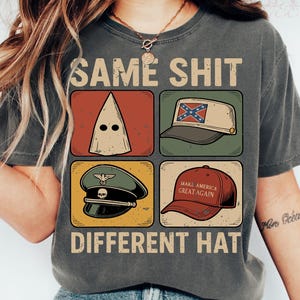 May include: Dark grey t-shirt with the text "SAME SHIT DIFFERENT HAT" above four images of hats. The hats include a white hood, a hat with a Confederate flag, a military hat, and a red baseball cap that says "MAKE AMERICA GREAT AGAIN."