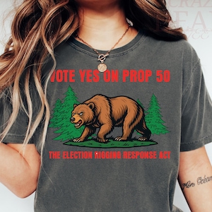 May include: Dark gray t-shirt with a graphic of a brown bear walking in front of green trees. The text "VOTE YES ON PROP 50" and "THE ELECTION RIGGING RESPONSE ACT" are printed in red.