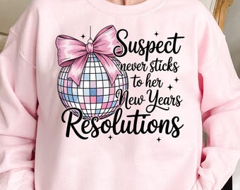 Puede incluir: Una sudadera rosa claro con un gráfico que presenta una bola de discoteca, un lazo rosa y el texto "Suspect never sticks to her New Years Resolutions". La bola de discoteca tiene cuadrados rosas, azules y blancos.