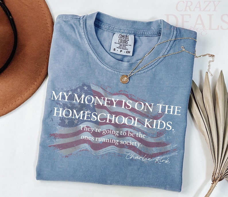Pu&ograve; includere: Una maglietta blu a maniche corte con la scritta "MY MONEY IS ON THE HOMESCHOOL KIDS." La maglietta presenta un disegno della bandiera americana usurata e la citazione "They're going to be the ones running society." di Charlie Kirk.