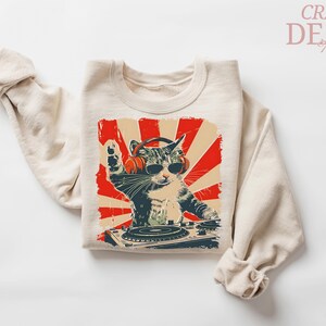 May include: Beige sweatshirt with a graphic of a cat DJ wearing headphones and sunglasses, set against a red and beige sunburst design. The cat is behind a turntable. The words "CRAZY DEALS" are in the upper right corner.