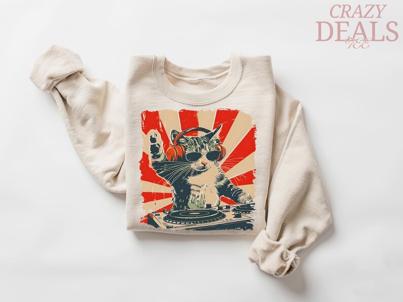 May include: Beige sweatshirt with a graphic of a cat DJ wearing headphones and sunglasses, set against a red and beige sunburst design. The cat is behind a turntable. The words "CRAZY DEALS" are in the upper right corner.