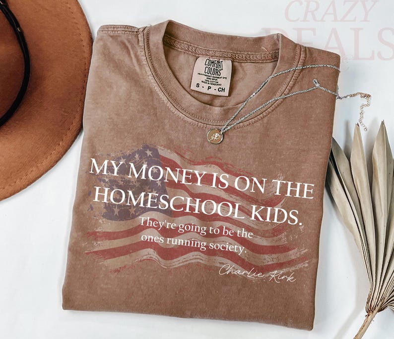 Pu&ograve; includere: Una maglietta marrone con la scritta "MY MONEY IS ON THE HOMESCHOOL KIDS. They're going to be the ones running society." e un disegno della bandiera americana. Una collana d'argento con un ciondolo &egrave; sulla maglietta.