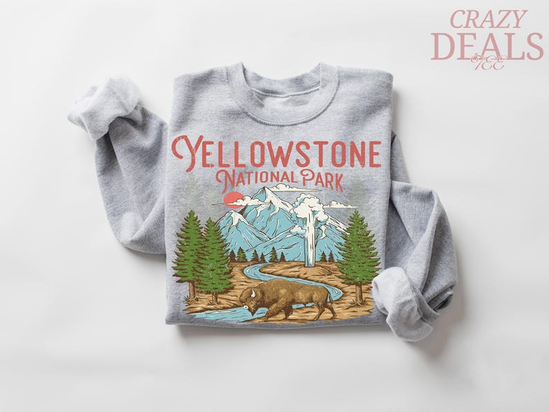 May include: Gray sweatshirt with a graphic of Yellowstone National Park. The design includes mountains, trees, a bison, and the text "Yellowstone National Park" in red. The sweatshirt has rolled-up sleeves.