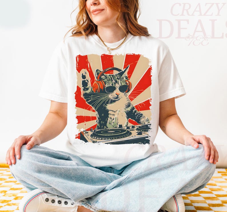 May include: White t-shirt with a graphic of a cat DJ wearing sunglasses and headphones, set against a red and beige retro backdrop. The cat is behind a DJ turntable, with its paw raised. The text "Crazy Deals" is visible.