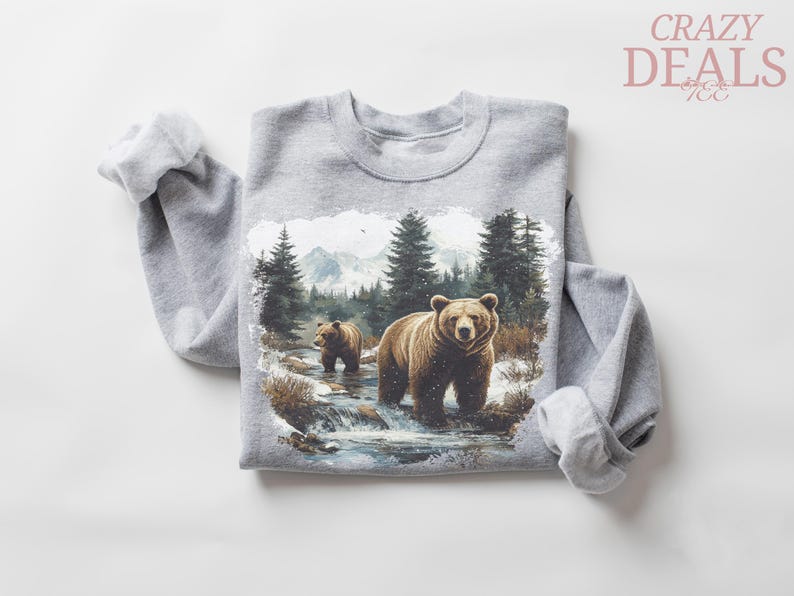 May include: A gray sweatshirt featuring a detailed illustration of two brown bears in a forest stream with evergreen trees and mountains in the background. The text "CRAZY DEALS" is in the upper right corner.