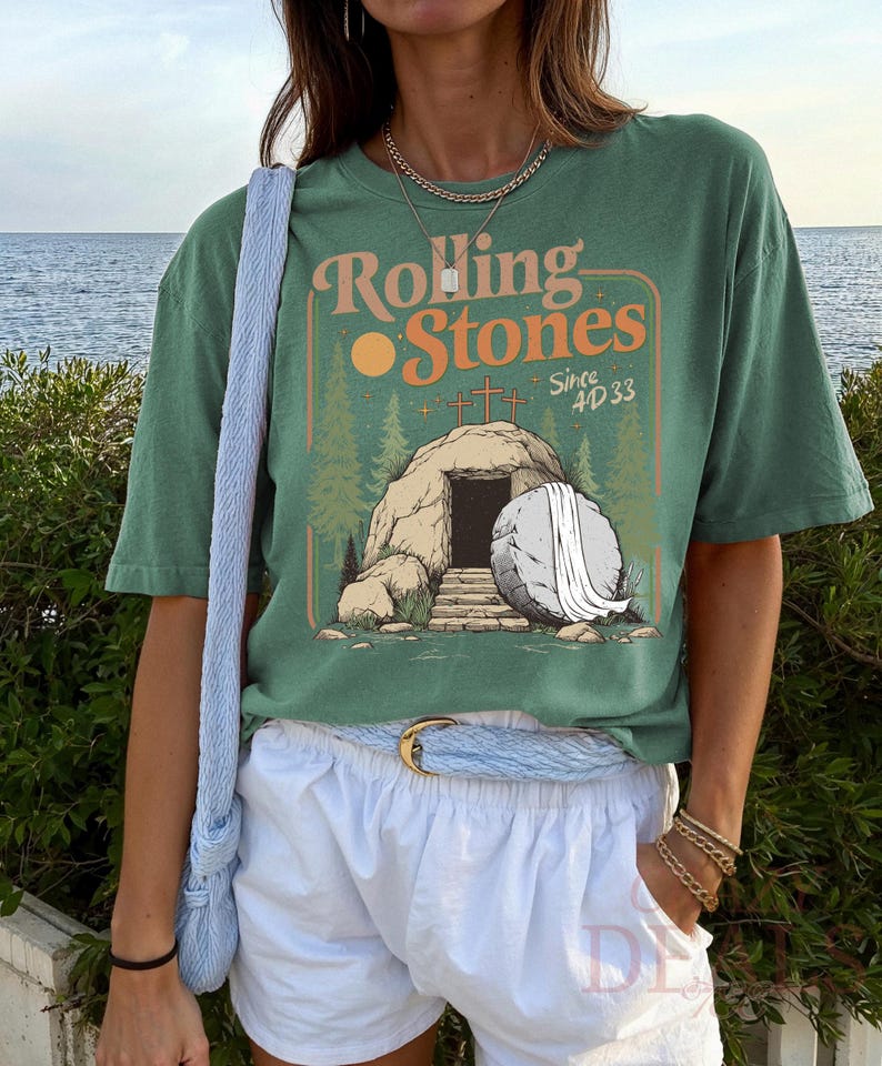 Pu&ograve; includere: T-shirt verde con la scritta "Rolling Stones Since 4D 33" in arancione e bianco. La grafica raffigura una tomba con croci, un sole e una pietra. La maglietta &egrave; abbinata a pantaloncini bianchi e una borsa blu.
