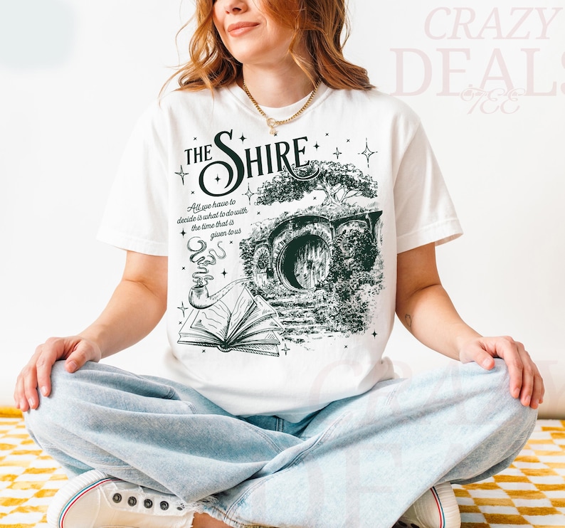 May include: White t-shirt featuring a green and black graphic of a hobbit hole with the text "THE SHIRE". The shirt also includes the quote "All we have to decide is what to do with the time that is given to us."