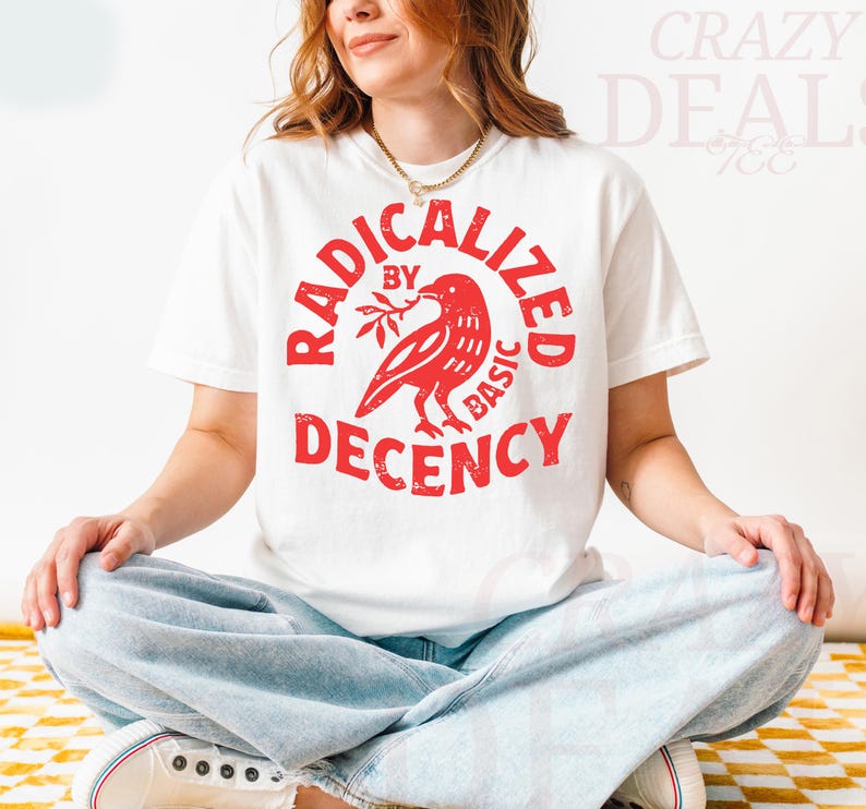 May include: White t-shirt with a red graphic that reads "RADICALIZED BY BASIC DECENCY" around a bird holding a branch. The person is wearing light blue jeans and white sneakers.
