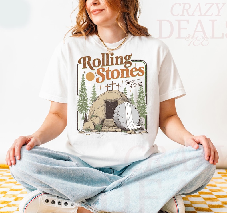 Pu&ograve; includere: T-shirt bianca con grafica di una tomba, pietra, alberi e la scritta "Rolling Stones Since AD 33" in marrone e verde. La maglietta ha girocollo e maniche corte.