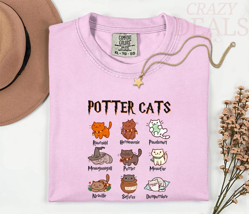 Pu&ograve; includere: T-shirt rosa chiaro con la scritta "POTTER CATS" e illustrazioni di gatti dei cartoni animati. La maglietta presenta vari personaggi di gatti con nomi come "Rawrnald" e "Hermeownie". Una collana d'oro con un ciondolo a forma di stella &egrave; drappeggiata sulla maglietta.