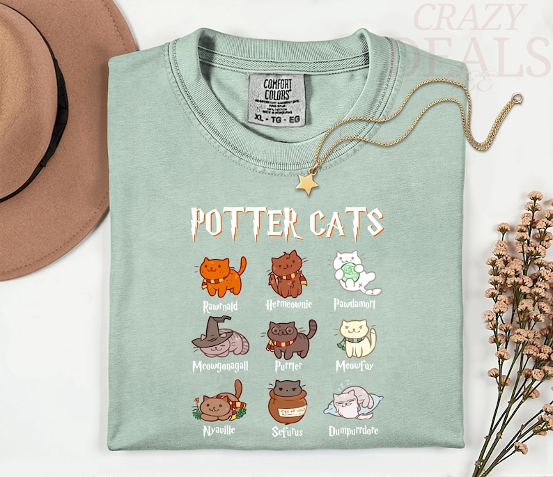 Pu&ograve; includere: Una maglietta verde chiaro con la scritta "POTTER CATS" e illustrazioni di gatti dei cartoni animati. I gatti sono vestiti con vari abiti. Una collana d'oro con un ciondolo a forma di stella &egrave; sulla maglietta.