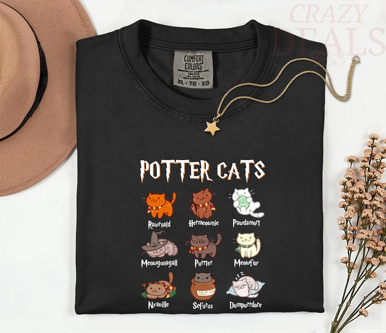 Pu&ograve; includere: T-shirt nera con la scritta "POTTER CATS" e illustrazioni di gatti dei cartoni animati. La maglietta presenta vari personaggi di gatti con nomi come "Rawrnald" e "Hermeownie". Una collana con ciondolo a stella dorata &egrave; drappeggiata sulla maglietta.