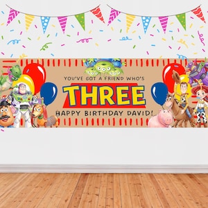 May include: A rectangular birthday banner featuring Toy Story characters including Buzz Lightyear, Woody, Jessie, Rex, and Mr. Potato Head. The text reads YOU'VE GOT A FRIEND WHO'S THREE HAPPY BIRTHDAY DAVID in yellow, red, and black lettering.