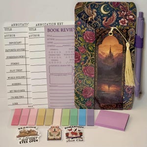 May include: A reading journal set with a decorative cover featuring roses, griffins, and a castle scene. Includes annotation sheets, sticky notes, bookmarks, a pen, and stickers with text: "Reading is Dreaming with Your Eyes Open" and "Romantasy Book Club."