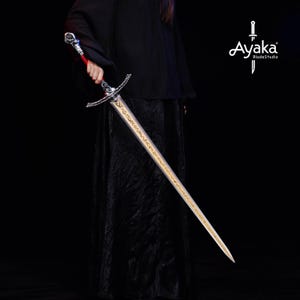 May include: A long, silver sword with a gold blade and ornate hilt is held against a black background. The hilt features a red grip and intricate detailing. The blade has gold inscriptions. The logo "Ayaka BladeStudio" is in the upper right corner.