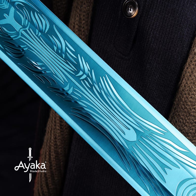 May include: Close-up of a blue sword blade with intricate etched designs. The blade has a reflective surface and is held against a dark background. The logo "Ayaka BladeStudio" is visible.