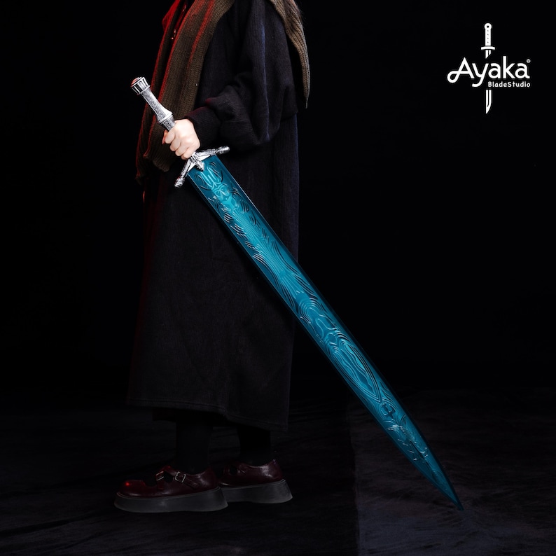 May include: A long, two-handed sword with a silver hilt and a vibrant blue blade. The blade features a unique pattern and is held by a person wearing dark clothing. The Ayaka Blade Studio logo is visible in the upper right corner.