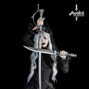 Puede incluir: Una espada y una daga plateadas con diseños ornamentados sobre un fondo negro. La espada tiene una guarda curva y una empuñadura detallada. La daga tiene una hoja recta y un mango a juego. El logotipo "Ayaka BladeStudio" es visible.