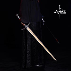 May include: A long, ornate sword with a silver hilt and a gold-colored blade. The sword is held by a person wearing a black robe. The image also shows a second sword and the text "Ayaka BladeStudio".