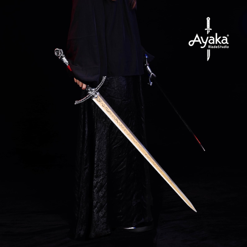 May include: A long, ornate sword with a silver hilt and a gold-colored blade. The sword is held by a person wearing a black robe. The image also shows a second sword and the text "Ayaka BladeStudio".